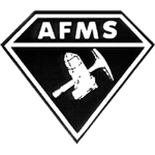 A black and white image depicting a stylized faceted gem features the letters AFMS above an image of a crystal and a hand tool similar to a pickaxe.